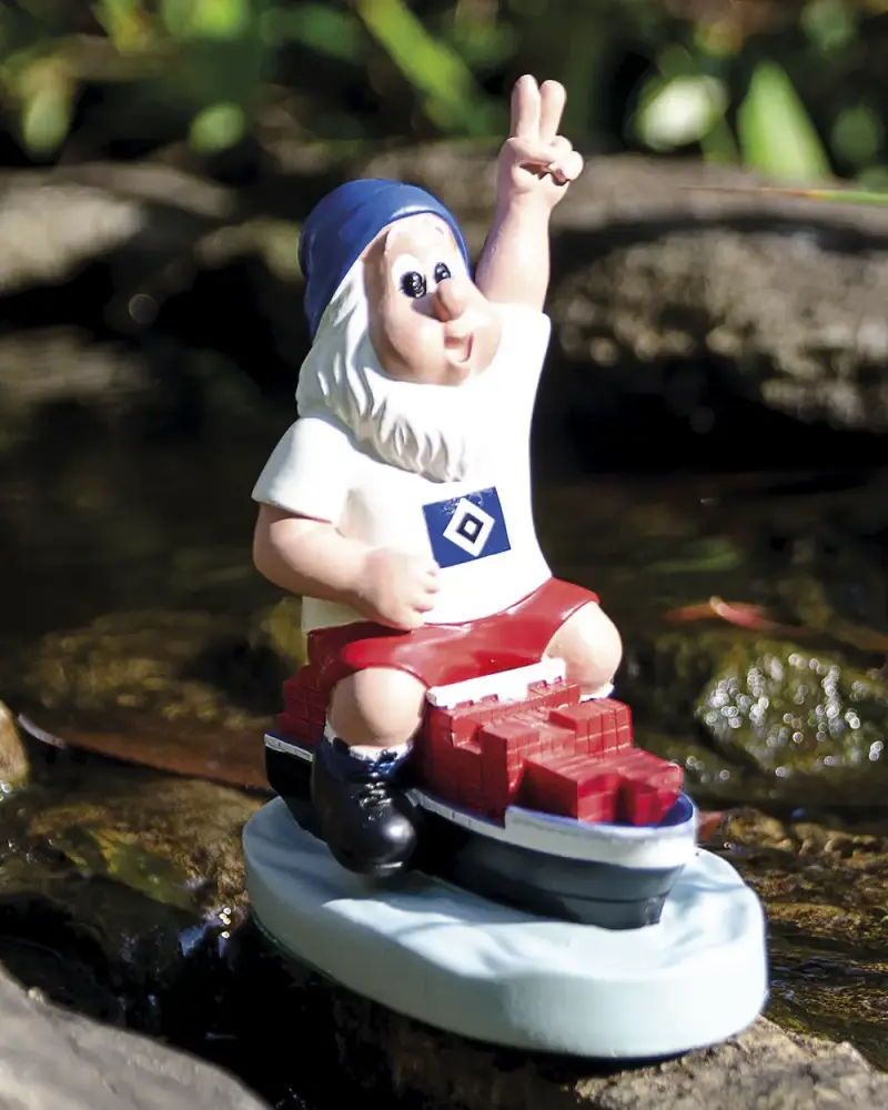 Gartenzwerg im Fußballtrikot mit Victory-Zeichen auf einem Miniatur-Containerschiff